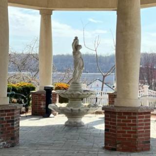A scenic view of a gazebo with a central fountain and surrounding columns, overlooking a serene landscape.