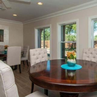 A cozy dining room with a round wooden table and upholstered chairs, surrounded by windows letting in natural light.