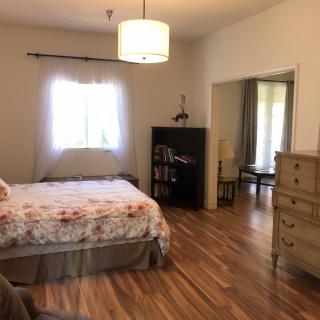 A cozy bedroom with wooden flooring, featuring a bed, dresser, and bookshelf.