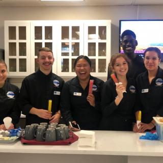A team of smiling people in uniforms preparing food in a kitchen.