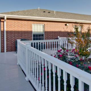 A sunny outdoor view of a building with brick walls, surrounded by a white fence and colorful flowers.
