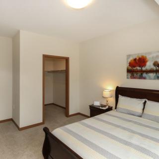 A cozy bedroom with a neatly made bed, a bedside lamp, and an open closet.