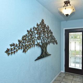 A decorative metal tree wall art piece adorns a blue entryway, complemented by a modern light fixture and a glass-paneled door.