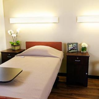 A minimalist bedroom featuring a single bed with wooden headboard, flanked by two nightstands and illuminated by sleek wall-mounted lights.