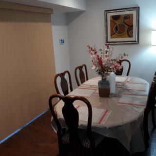 A dining room with a table set for six, decorated with flowers and adorned by a piece of artwork on the wall.