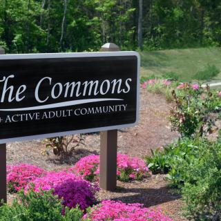 A sign reading 'The Commons: An Active Adult Community' surrounded by colorful flowers.