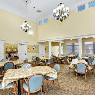 A spacious dining area with multiple tables and chairs, illuminated by elegant chandeliers.
