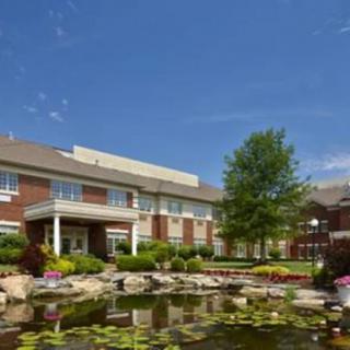 A scenic view of a brick building with a landscaped garden and pond in the foreground.