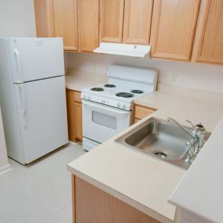 A compact kitchen with wooden cabinets, a fridge, stove, and sink.