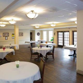 A well-lit dining area with round tables and chairs, covered with white tablecloths.