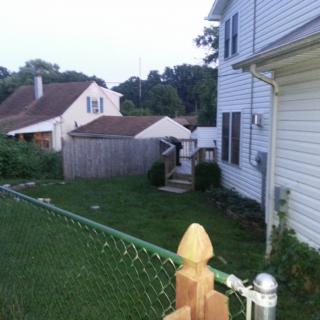 A suburban backyard with a white house and a chain-link fence during the evening.
