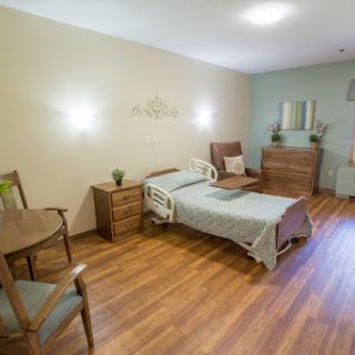 A well-furnished hospital room featuring a single bed, wooden flooring, and comfortable seating.