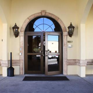A building entrance featuring double glass doors and an arched design, flanked by decorative lights.