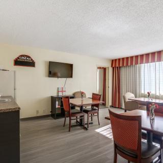 A bright hotel dining area with tables, chairs, and a wall-mounted TV.
