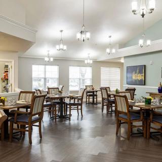 A well-lit dining area with elegantly arranged tables and chairs, featuring chandeliers and wooden flooring for a cozy ambiance.