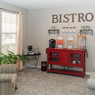 A cozy bistro-themed corner with a beverage station, featuring a coffee machine and drink dispensers on a red cabinet.