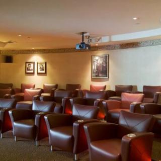 A cozy theater room with rows of leather chairs and a ceiling-mounted projector.