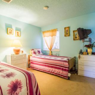 A cozy bedroom with twin beds, decorated in soft colors, featuring natural light from a window with drapes.