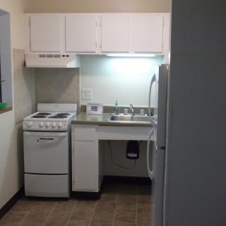 A compact apartment kitchen with basic white appliances and cabinetry.