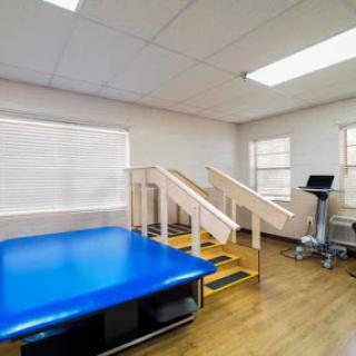 A spacious physical therapy room equipped with a blue exercise mat and stairs for rehabilitation exercises.