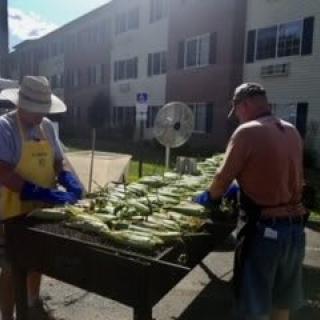 People grilling corn outdoors at a summer event.