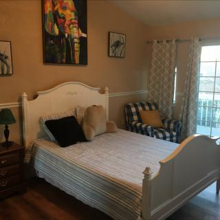 A cozy bedroom with a white bed and a patterned chair, featuring wall art and soft lighting.