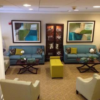 A modern lobby with blue sofas, white armchairs, and abstract wall art creates a welcoming waiting area.