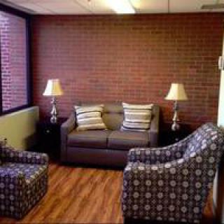 A cozy living room with a sofa, two patterned armchairs, and two lamps against a brick wall.