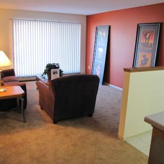 A cozy living room featuring a comfortable sofa, a lamp for warm lighting, and decorative wall art against an orange accent wall.