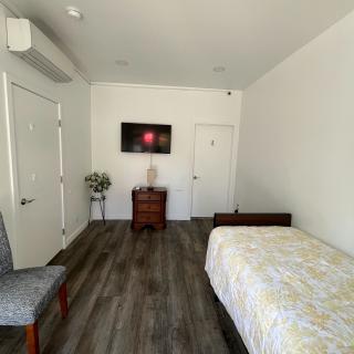 A minimalist bedroom with a single bed, hardwood floor, and a TV mounted on the wall.