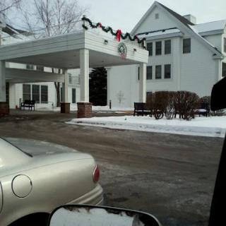 A winter scene featuring a decorated entrance to a building, with snow covering the ground and a parked car in the foreground.