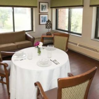 A cozy dining area with a round table set for two, featuring a sofa and large windows.