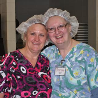 Two healthcare professionals smiling in scrubs and hairnets.
