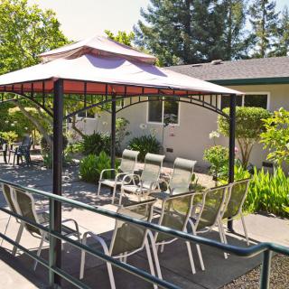 A cozy outdoor patio with a gazebo, chairs, and table surrounded by lush greenery.