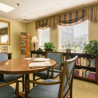 A well-lit meeting room with a wooden table, chairs, and a bookshelf near the windows.