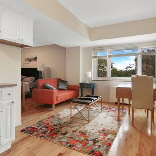 A cozy open-plan living space with a sofa, dining table, and kitchen area, featuring a large window with a scenic view.