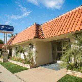 A sunny day view of a motel with a red tile roof and blue signage.