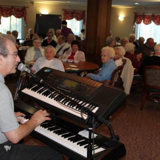 A musician performs on a keyboard for an attentive audience in an indoor setting.