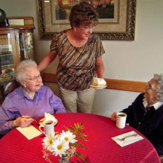 A caregiver serving cake to two elderly women during a social gathering at a cozy cafe.