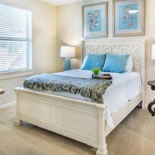 A cozy bedroom featuring a white bed with blue accent pillows, decorative artwork, and soft lighting.