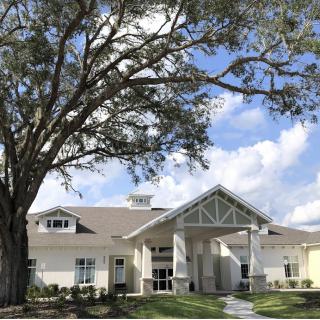 A modern building with a large tree in front, set against a partly cloudy sky.