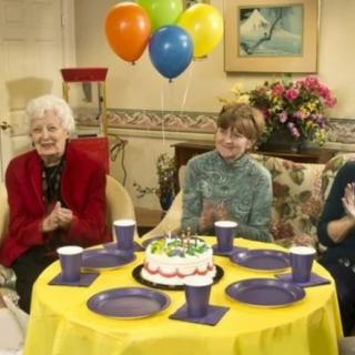 A group of people celebrating a birthday with cake and balloons.