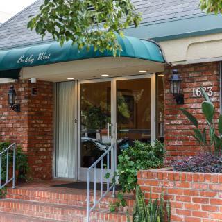 A cozy restaurant entrance with a green awning and brick exterior, surrounded by plants.