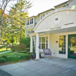 A sunny day view of a building entrance with neatly landscaped surroundings and a paved walkway.