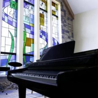 A piano in a room with large stained glass windows.