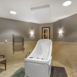 A modern bathroom featuring a walk-in tub with wall lights and tiled flooring.