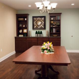 A dining room with a central wooden table, adorned with a floral centerpiece. Bookshelves and a decorative mirror enhance the background ambiance.