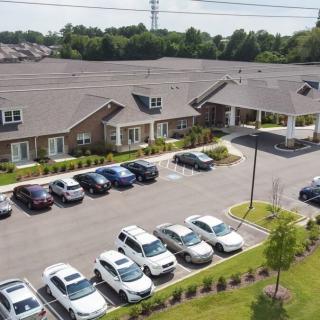 Aerial view of a parking lot with several cars in front of a large building and surrounding greenery.
