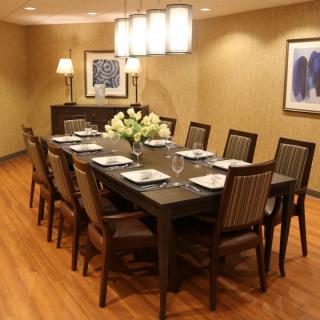 An elegant dining room with a large table set for eight, featuring stylish lighting and floral centerpiece.