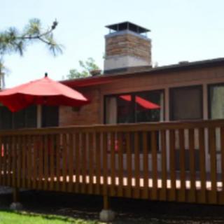 A house with a wooden deck featuring a red umbrella and a chimney.